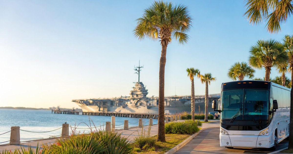 The USS Lexington docked on the Corpus Christi bay waterfront on a clear morning with a charter coach bus parked nearby.
