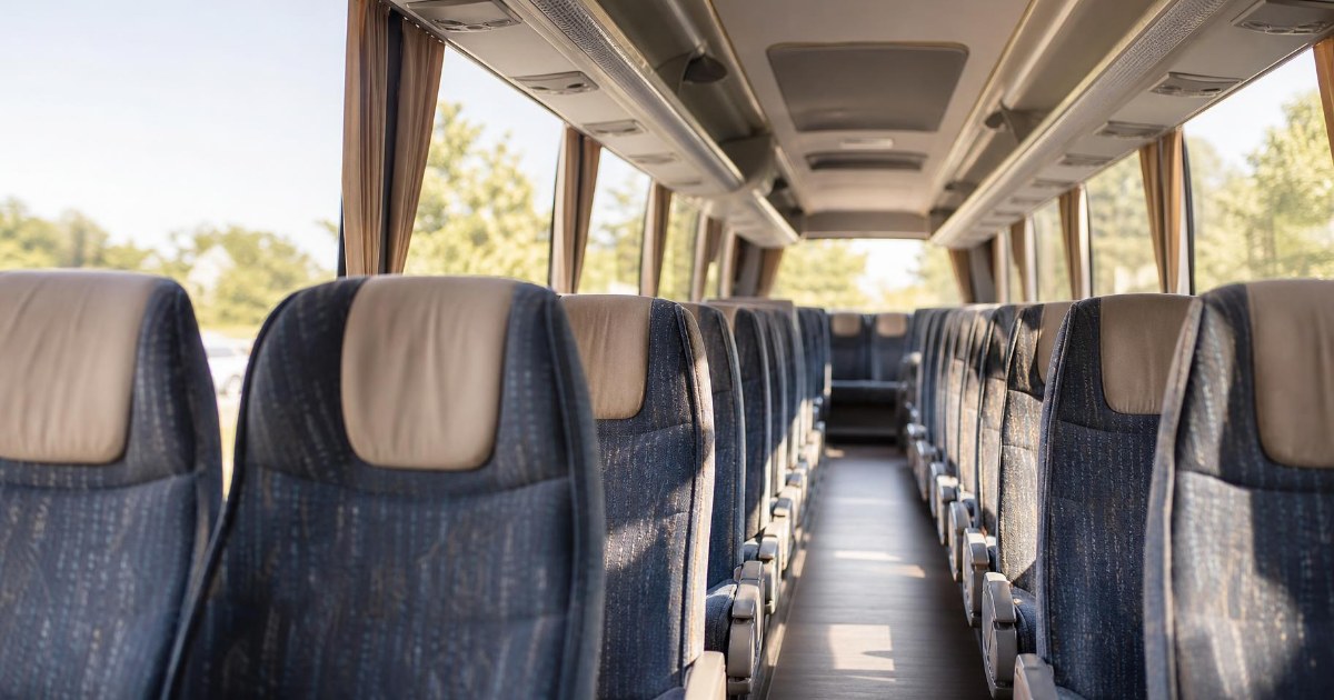Rows of cushioned reclining seats along the aisle inside a full-size charter bus in soft daylight.