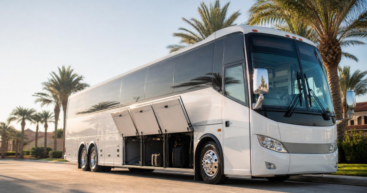 A full-size motorcoach parked at a sunny curb with its luggage bay doors open beneath the raised passenger deck.